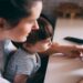 A parent using a smartphone while supervising a child, highlighting online safety and AI-related privacy risks.