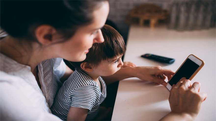 A parent using a smartphone while supervising a child, highlighting online safety and AI-related privacy risks.